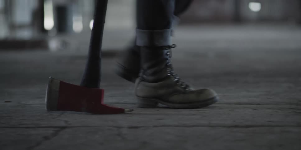 The feet of a person as they walk along dragging an axe beside them