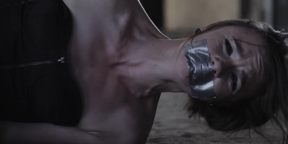 A woman in a room crying with her mouth duct tape with a wall in the background