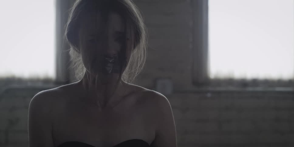 Someone joins a woman as she sits in a darkened room