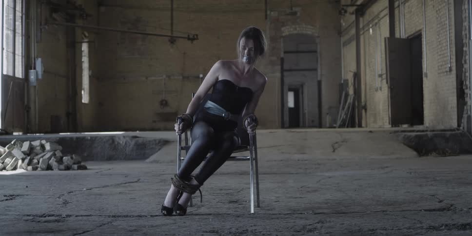 A woman tied to a chair is struggling to escape