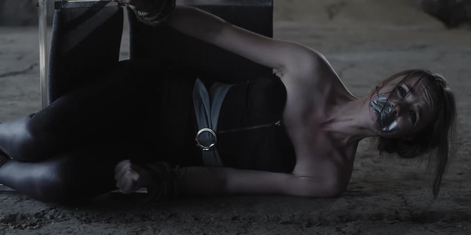 A woman with duct tape over her mouth struggles while tied to a tipped over chair