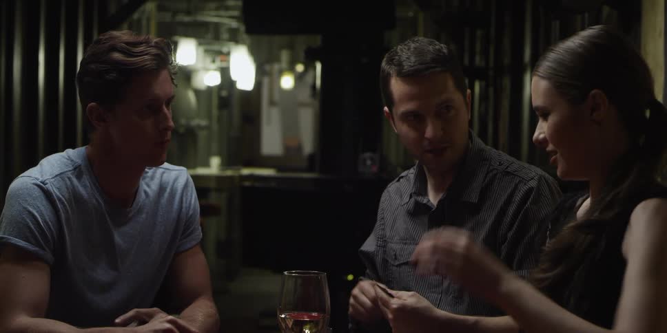A woman joins two men who are sitting at a table playing a card game