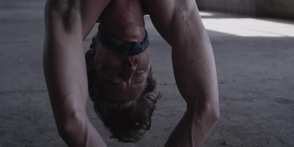 A man in a room tied upside down with a wall in the background
