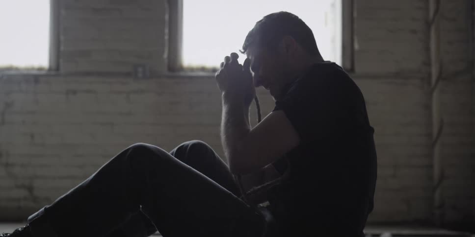 A man holds a rope as he cries on the floor of a dilapidated building