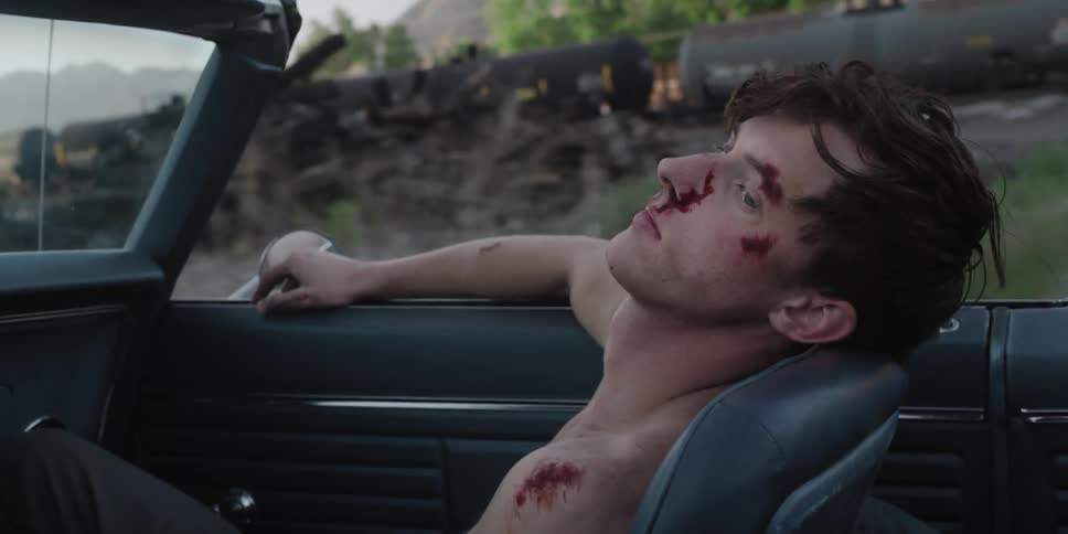 Young injured bloody man sitting on the seat of a convertible car driving on a rural area