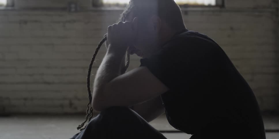 A man sitting on the floor cries in anguish while holding a rope in his hands