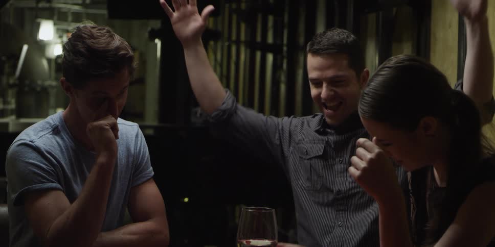 Three friends are playing card indoors as one of them applauds after winning the game