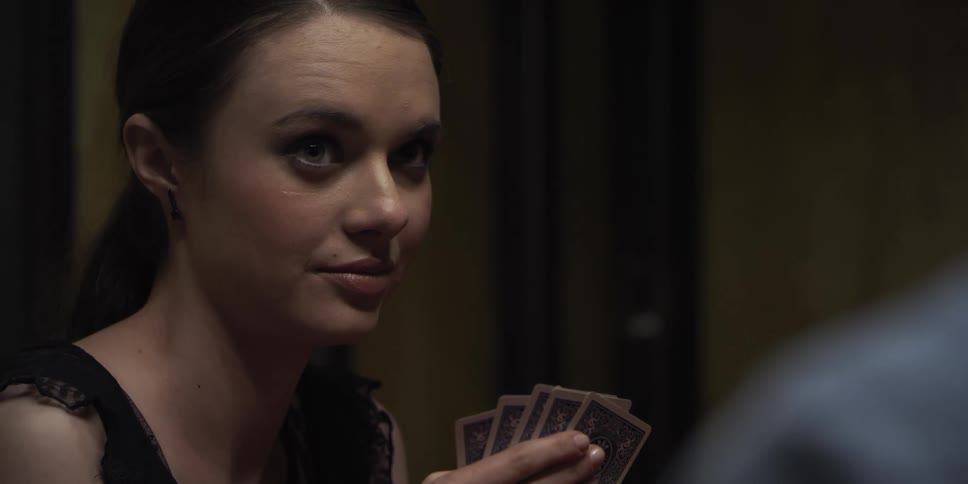 A woman looks at cards in her hands and then looks across at a person she is playing with