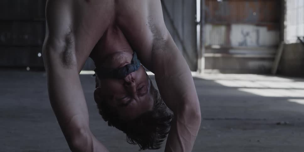 A man struggles to see while tied up and hanging upside down in a warehouse