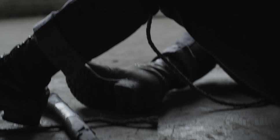 A man with an axe at his feet sits on a concrete floor in a building and holds a rope and cries