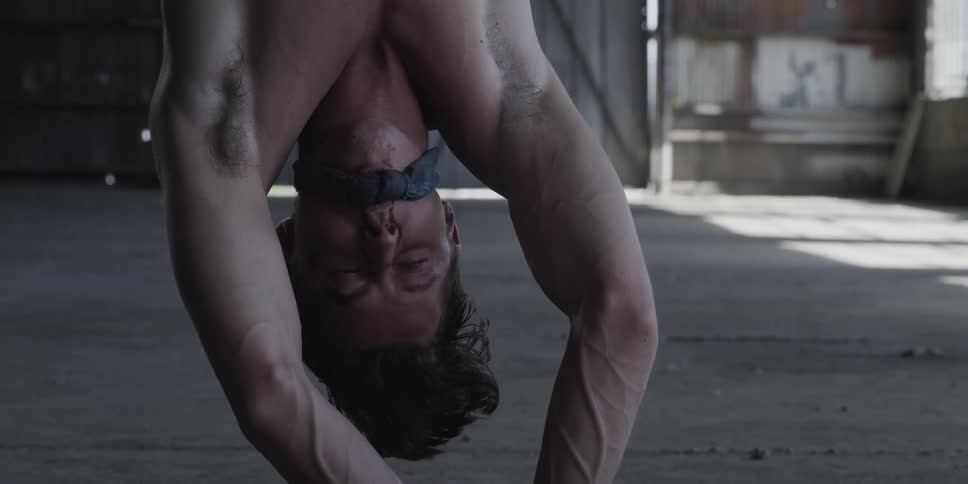 A man is moving his mouth as he hangs upside down by his feet