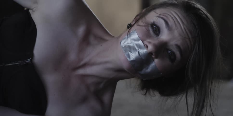 A woman is lying on her side with duct tape on her mouth and looking at the camera