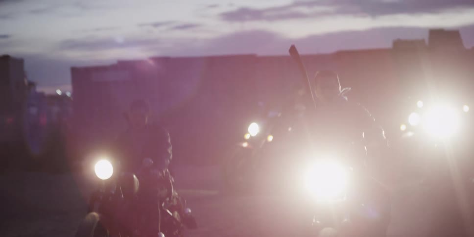 People riding motorcycles with buildings the sky and clouds in the background