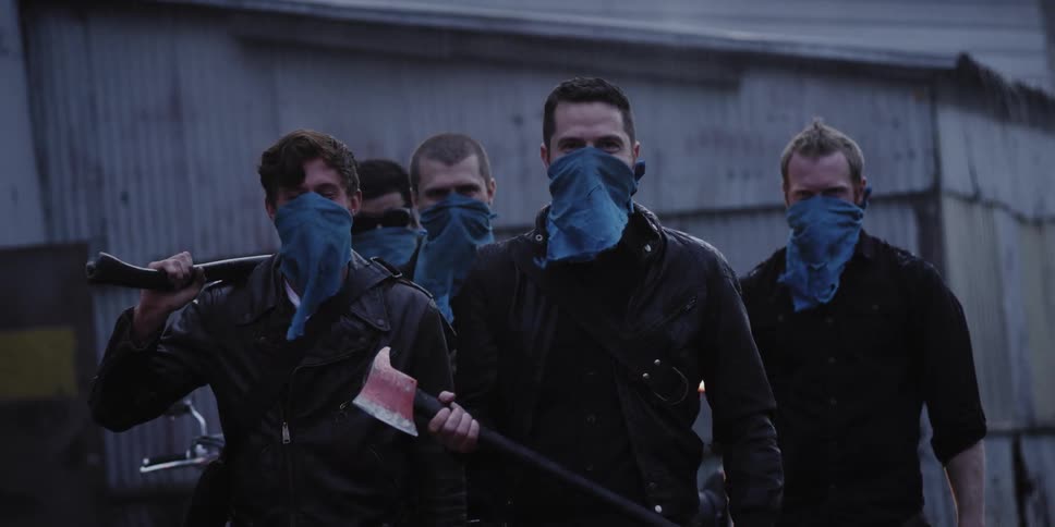 A group of armed men stands waiting in front of a building