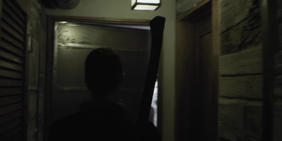 A man with an ax walking in a hallway and opening a door to a room with a woman looking at a painting