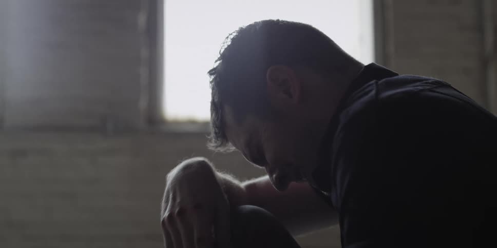 A man in a room holding a rope and crying with a wall and window in the background