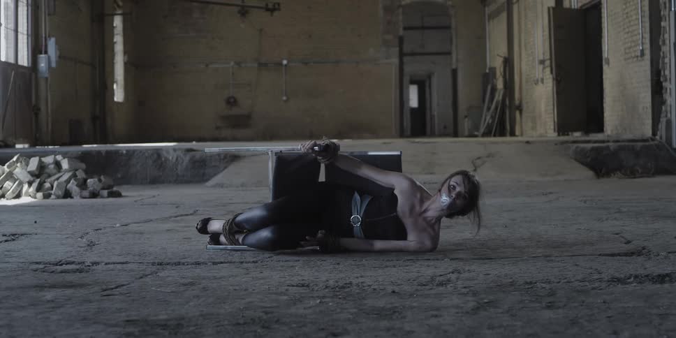 Scared gagged woman laying on the floor tied to a chair inside a warehouse