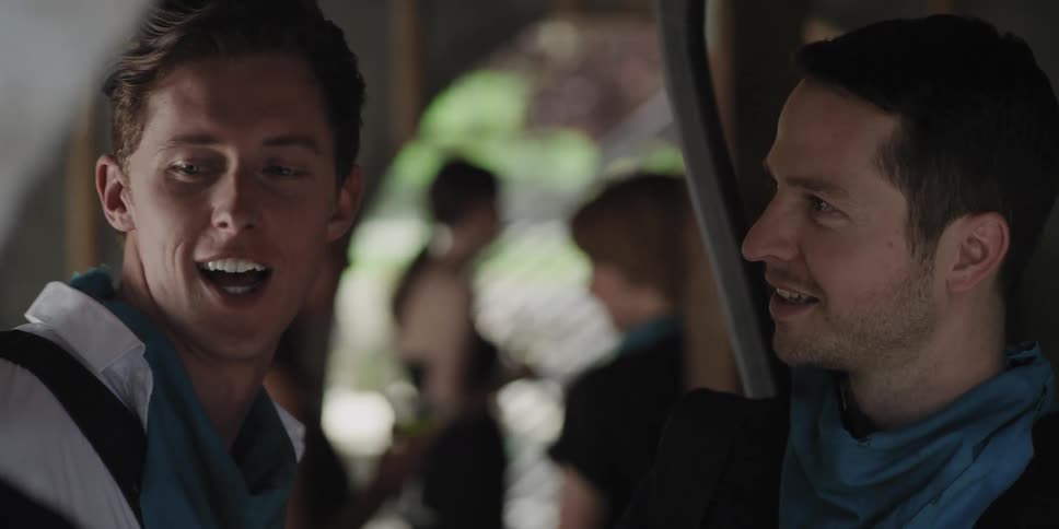 Men greet each other with smiles and a hug at a party while one carries long handled item across back