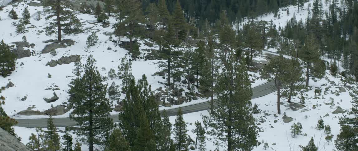 A car drives through a snow-covered forest in the mountains