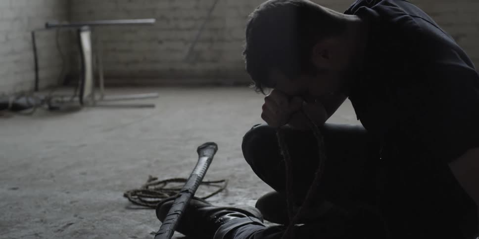 A man sitting on a concrete floor with an ax crying