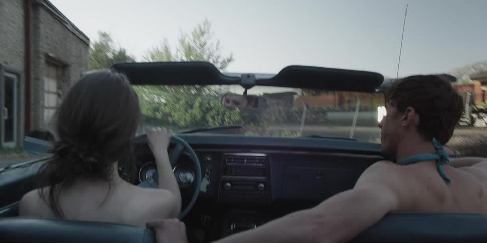 A man and woman are driving in a car through a parking lot