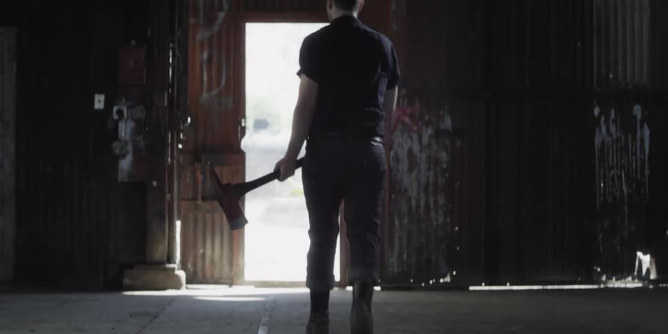 A man in a room walking and holding an ax with a wall and doorway in the background