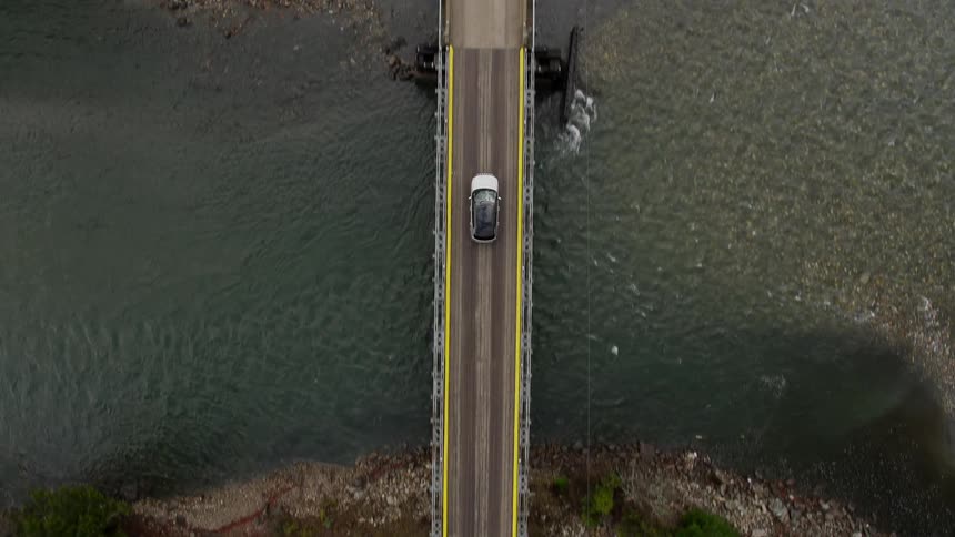 A vehicle drives on a narrow bridge over a river