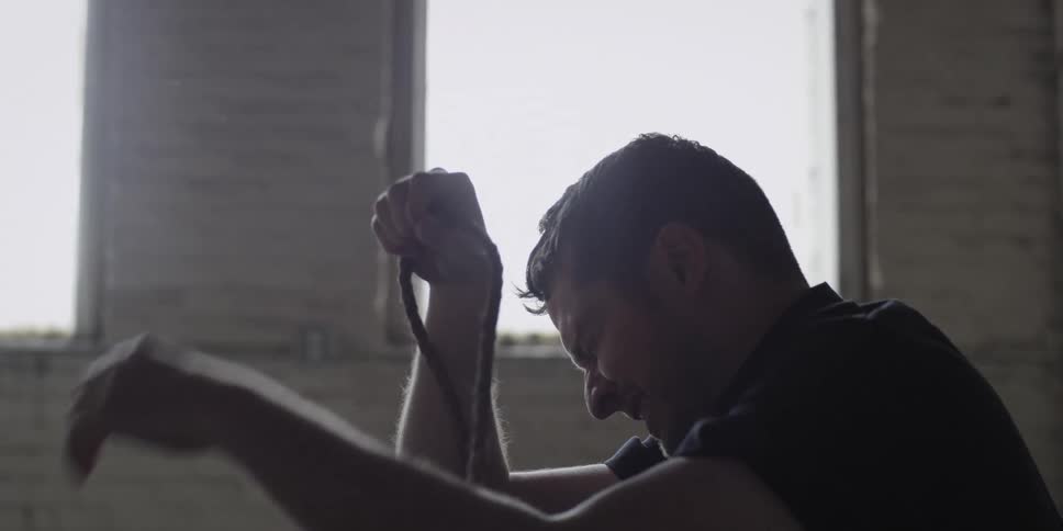 A man in a room holding a rope and crying with a wall and window in the background