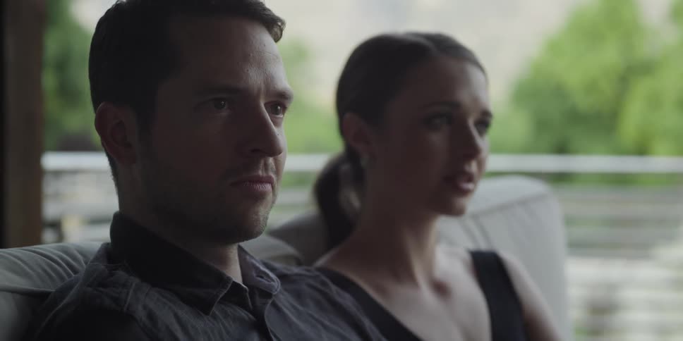 A man and a woman sitting on a couch with trees and railing in the background