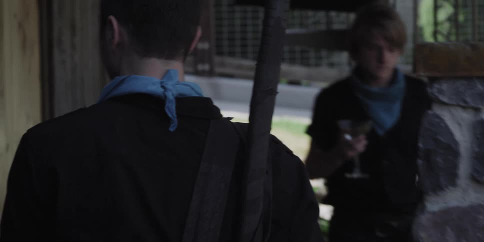 A man carrying a large pole on his back looks around at people drinking wine at an event before walking up some stairs