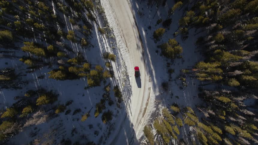 Aerial view of red car driving on snowy road through forest