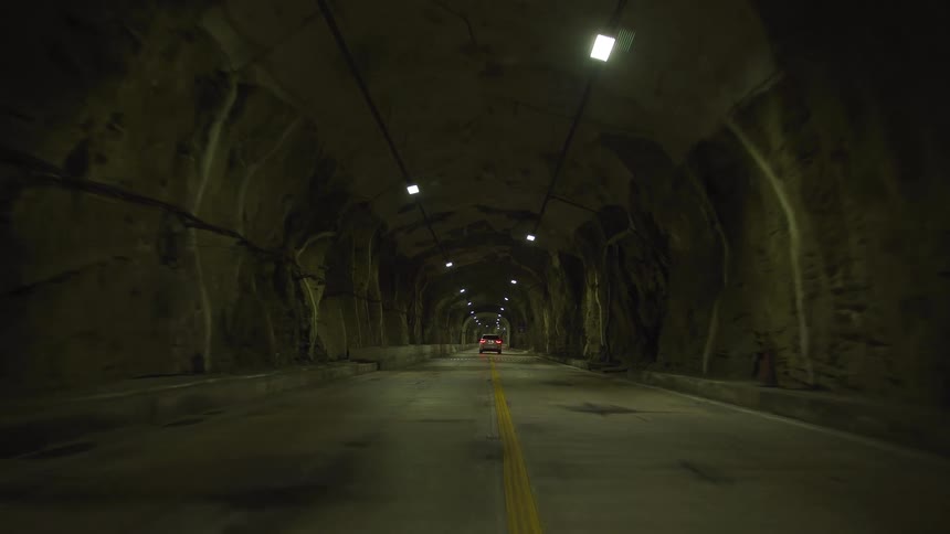 Car drives down long tunnel lit by ceiling lights