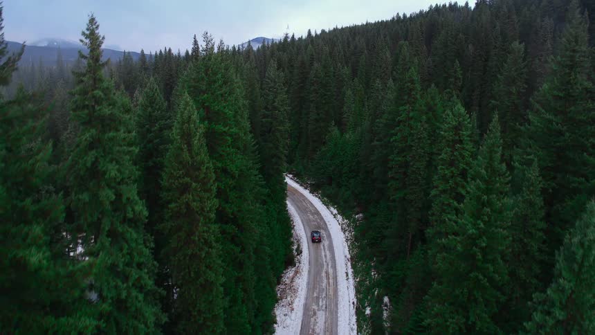 A car travels on a snow dusted mountain road through evergreen trees
