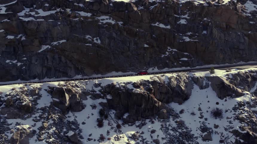 A car is driving on a road near the edge of a mountain