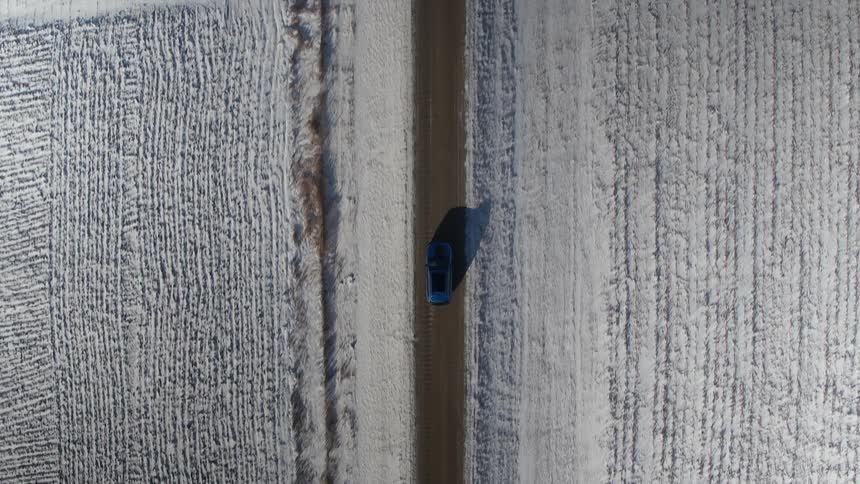Blue car driving down a road on a snow covered landscape