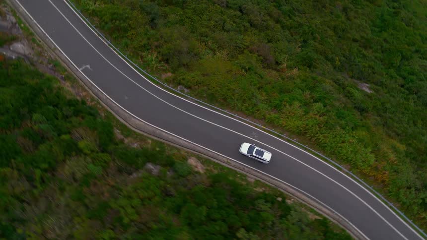 Aerial view of a white car traveling on a road surrounded by trees