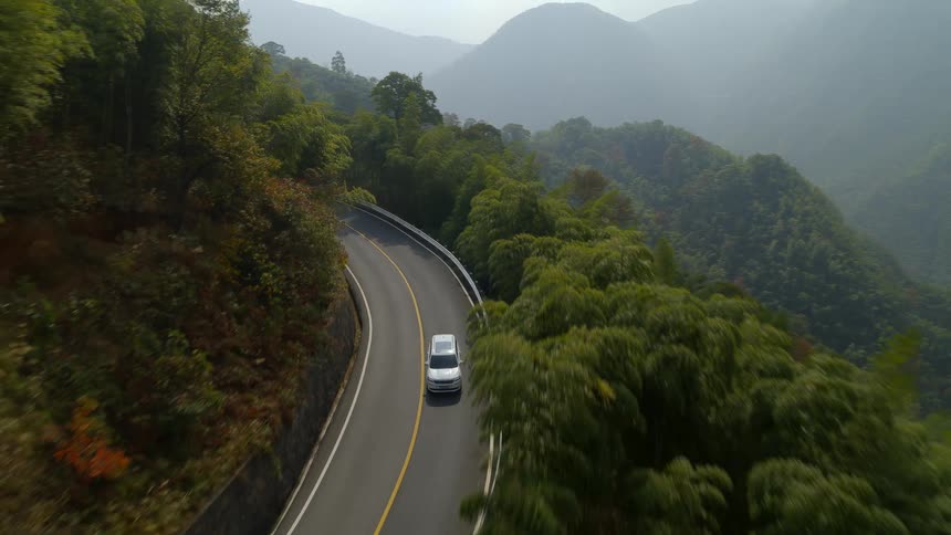 Aerial view of a car driving on the road in the mountains through the forest
