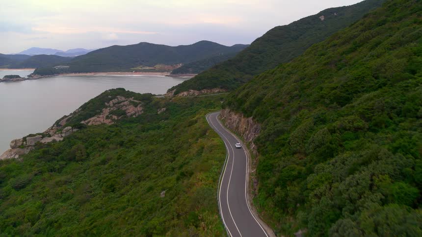 A vehicle driving on a road near a cliff with the sky and clouds in the background