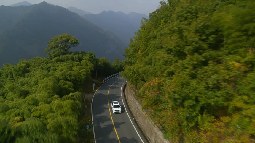 A white van travels on a mountain road with a mountain range in the distance
