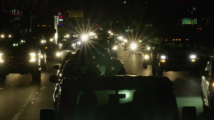 A highway with vehicles signs and streetlights with buildings in the background