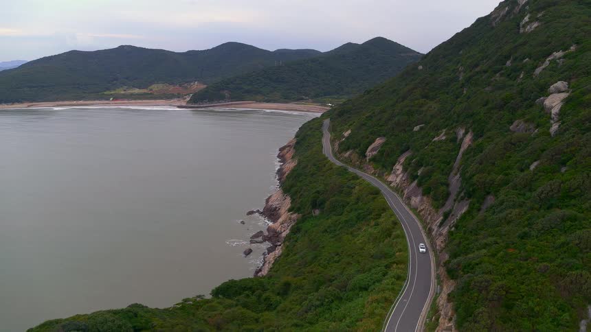 A vehicle driving on a road near a cliff with the sky and clouds in the background