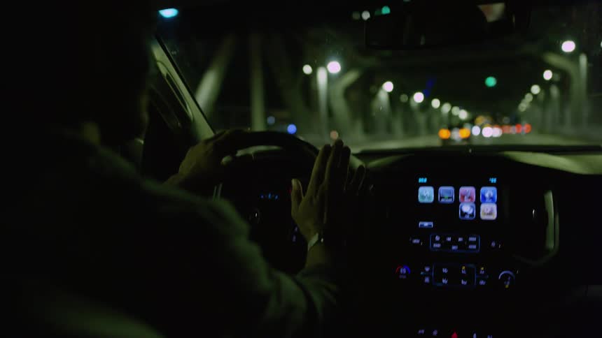 Man listening to music while driving a car down a bridge at night