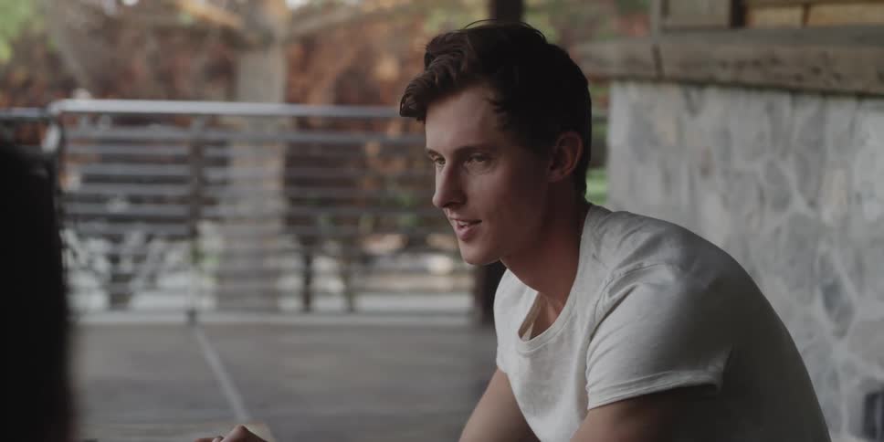 A man is sitting and talking to someone offcamera while outdoors during the day