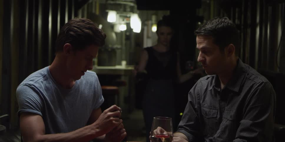 A woman brings drinks over to two men sitting playing cards