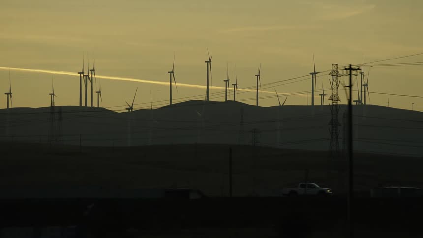 Vehicle driving near the turbines on a wind farm on the hills at sunset