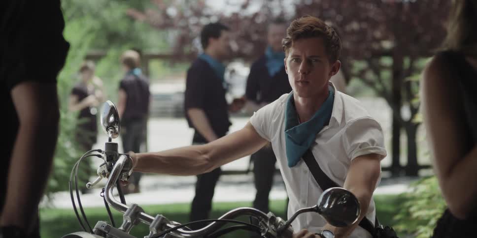 Man stops motorcycle and looks around party before smiling