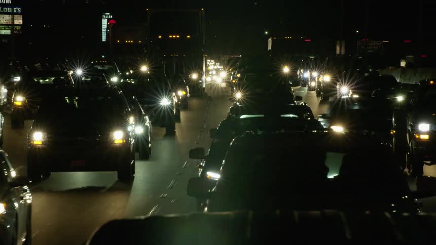 A highway with vehicles signs and streetlights with buildings in the background