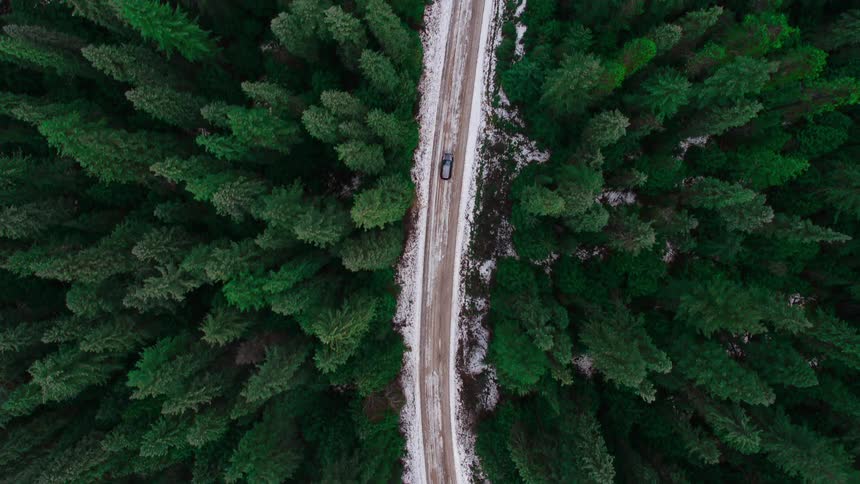Aerial view of a black van traveling on a snow covered forest road