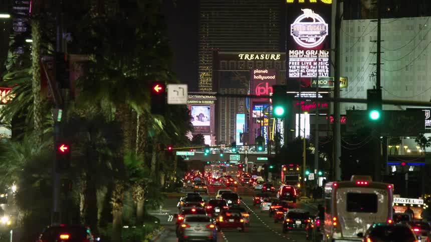 Vehicles driving down a busy city street past hotels at night