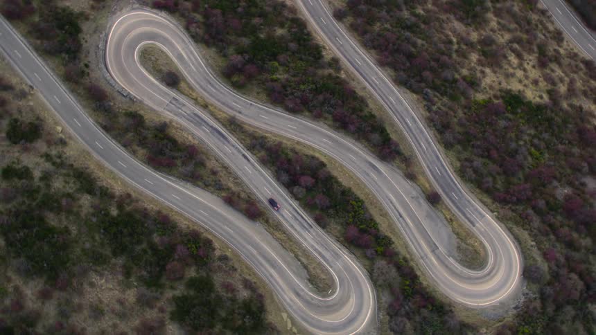 An aerial view of a vehicle driving on a twisty road in a large flat area